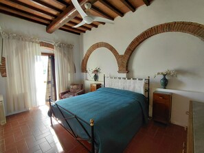 Een slaapkamer met een bed, een stoel, een nachtkastje, een vaas en een plafondventilator.