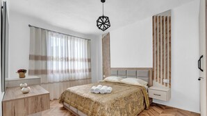 A modern bedroom with a bed, bedside tables, a window with curtains, and a hanging light fixture.