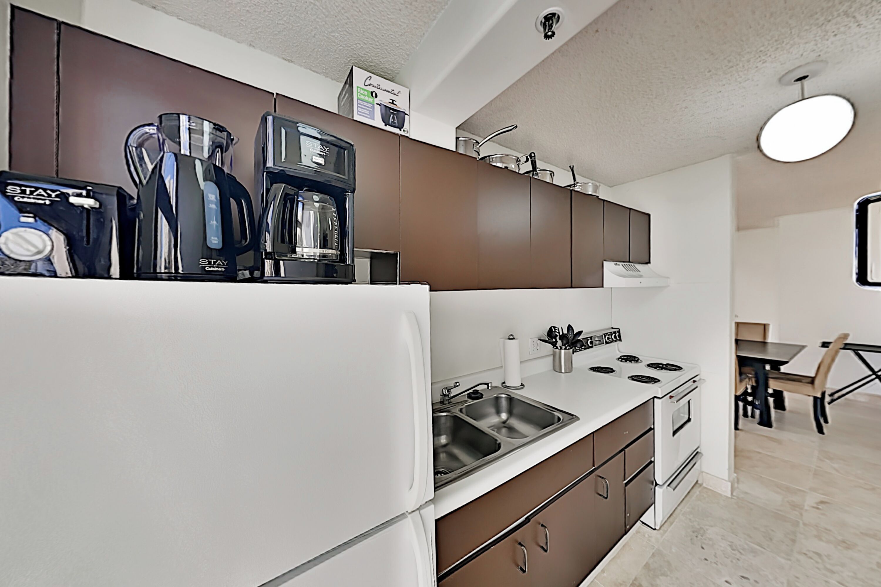 Una cocina moderna con un refrigerador blanco, un lavamanos de acero inoxidable y una estufa. Hay armarios sobre la encimera y una cafetera a la izquierda.