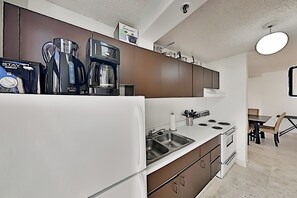 A modern kitchen with a white refrigerator, stainless steel sink, and a stove. There are cabinets above the counter and a coffee maker on the left. - Waikiki Banyan Corner Unit w/ In-Unit W/D & Parking (Honolulu)