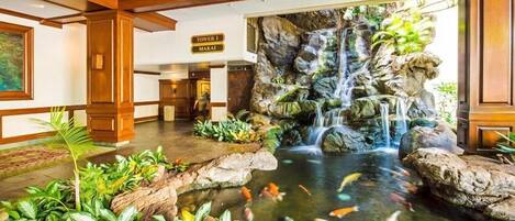 A lobby with a koi pond, a waterfall, and a sign for 'Tower 1 Marai'.
