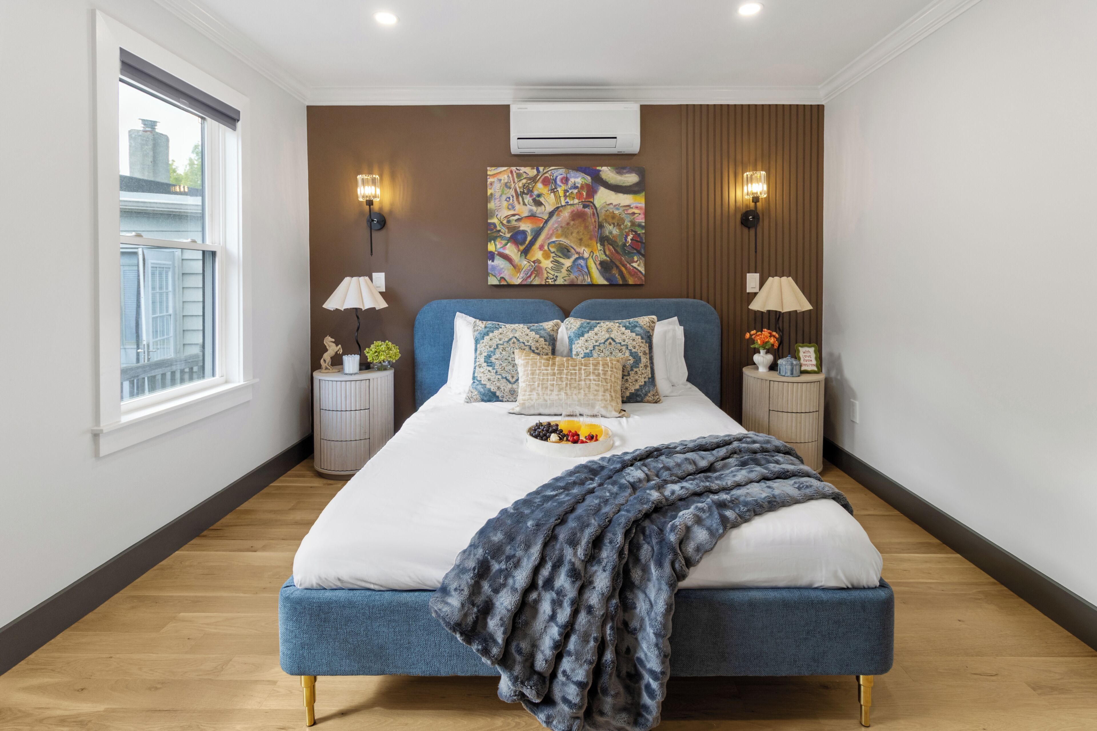 Een moderne slaapkamer met een groot bed, twee nachtkastjes, een raam en een wandairconditioner.