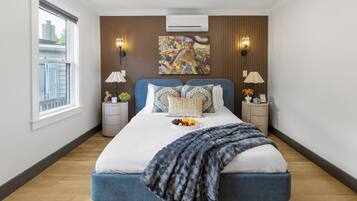 Een moderne slaapkamer met een groot bed, twee nachtkastjes, een raam en een wandairconditioner.