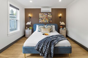 Een moderne slaapkamer met een groot bed, twee nachtkastjes, een raam en een wandairconditioner.