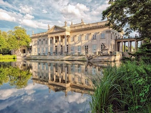 Ein klassizistisches Gebäude mit einer symmetrischen Fassade, großen Fenstern und Spiegelung im Wasser.