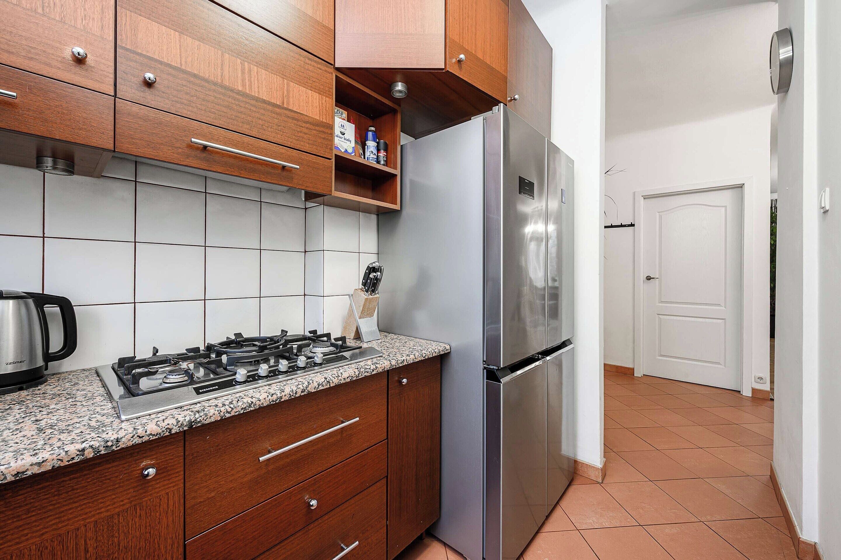 A kitchen with wooden cabinets, a stainless steel refrigerator, a gas stove, and a coffee maker.