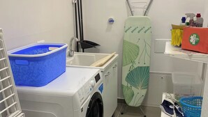 A laundry room with a washing machine, an ironing board, and various cleaning supplies. - "La Brogna" Apartment - Downtown Mazara del Vallo (Mazara del Vallo)