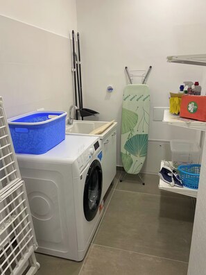 A laundry room with a washing machine, an ironing board, and various cleaning supplies. - "La Brogna" Apartment - Downtown Mazara del Vallo (Mazara del Vallo)