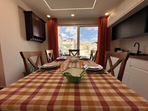 A dining area with a checkered tablecloth, wooden chairs, and a view of buildings through large windows. - "La Brogna" Apartment - Downtown Mazara del Vallo (Mazara del Vallo)
