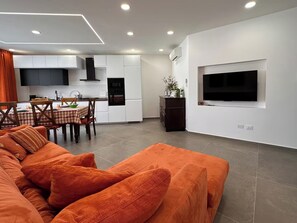 A modern living space with a sofa, dining area, kitchen, and a TV mounted on the wall. - "La Brogna" Apartment - Downtown Mazara del Vallo (Mazara del Vallo)
