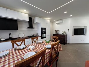 A modern kitchen with white cabinets, a black range hood, and a dining area with a checkered tablecloth. - "La Brogna" Apartment - Downtown Mazara del Vallo (Mazara del Vallo)