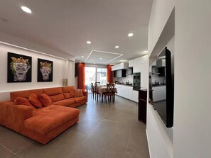 A modern living room with a sofa, a dining area with chairs, and a kitchen with cabinets and appliances. - "La Brogna" Apartment - Downtown Mazara del Vallo (Mazara del Vallo)