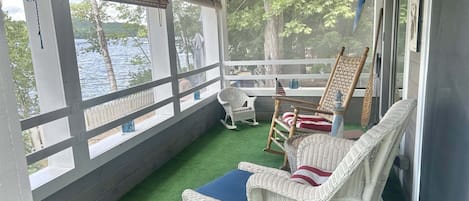 Varanda coberta com móveis de vime, vista para a água e um relógio na parede.