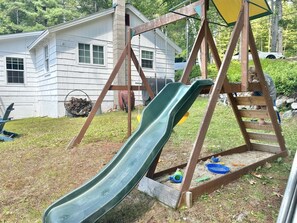 A backyard with a wooden swing set and a green slide.