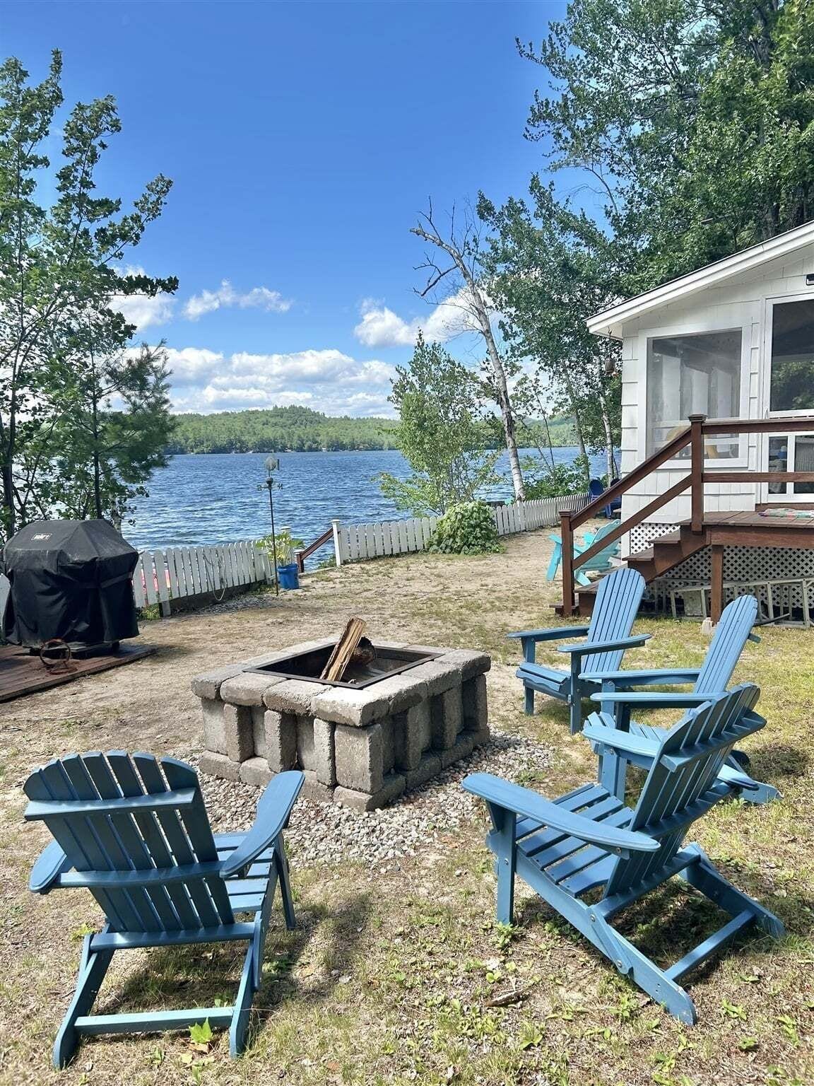 A lakeside deck with Adirondack chairs, a fire pit, and a covered grill area.