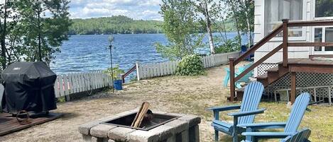 A lakeside deck with Adirondack chairs, a fire pit, and a covered grill area.