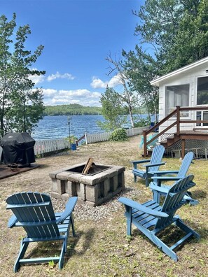 Um deck à beira do lago com cadeiras Adirondack, uma lareira e uma área de churrasqueira coberta.