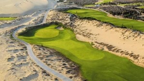Golfkenttä, jossa on hiekkabunkkereita, vesieste ja mutkitteleva polku.