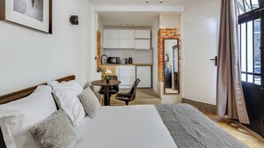 A hotel room with a bed, a small table with chairs, a kitchen area, and a view through a door. - Charming Studio 2P - Canal Saint Martin (Paris)