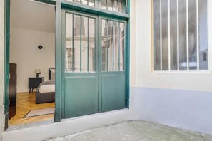 A room with a green door, a bed, a nightstand, and a window with vertical blinds. - Charming Studio 2P - Canal Saint Martin (Paris)