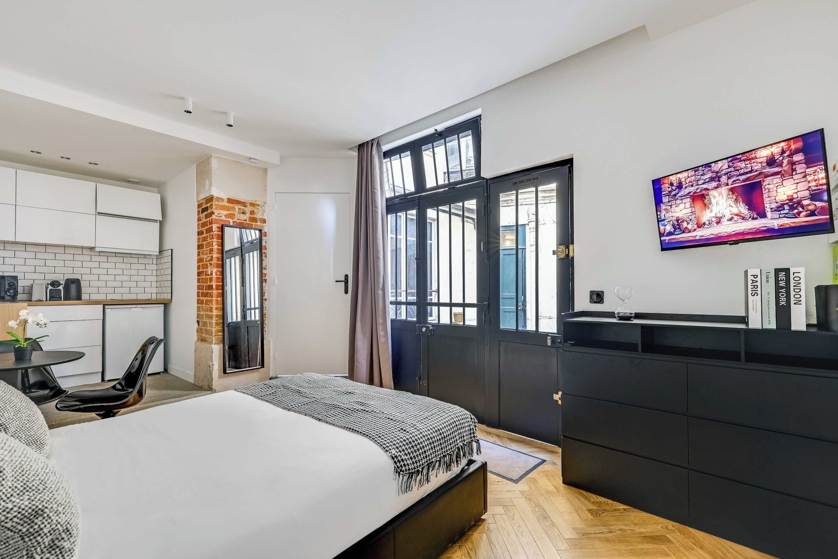 Une chambre d’hôtel moderne équipée d’un lit, d’un petit coin cuisine, d’une table à manger et d’une grande fenêtre.