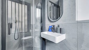 A modern bathroom with a glass shower enclosure, a white sink, and a round mirror. - Charming Studio 2P - Canal Saint Martin (Paris)