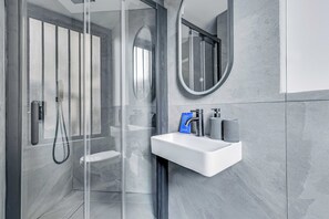 A modern bathroom with a glass shower enclosure, a white sink, and a round mirror. - Charming Studio 2P - Canal Saint Martin (Paris)