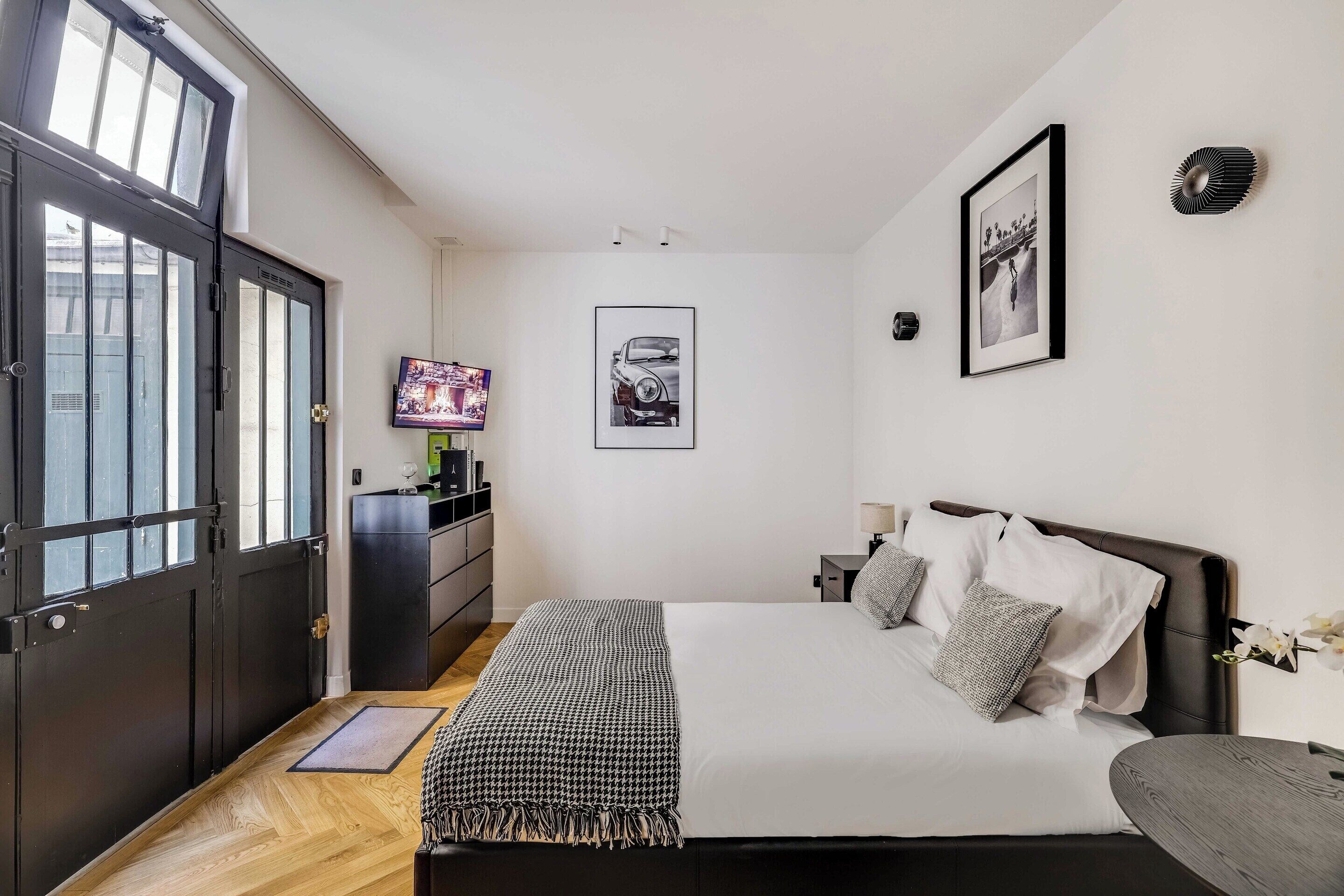 A bedroom with a bed, a TV, a dresser, and a door with windows.