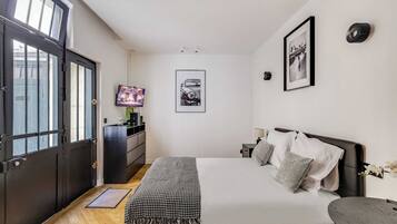 Un dormitorio con cama, televisor, cómoda y una puerta con ventanas.