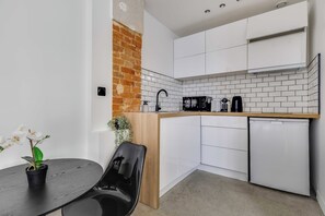 A compact kitchen with white cabinets, a brick accent wall, and a small dining area with a table and chair. - Charming Studio 2P - Canal Saint Martin (Paris)