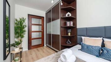 Quarto com cama, mesa de cabeceira, espelho, guarda-roupa e planta em vaso.