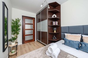 Quarto com cama, mesa de cabeceira, espelho, guarda-roupa e planta em vaso.