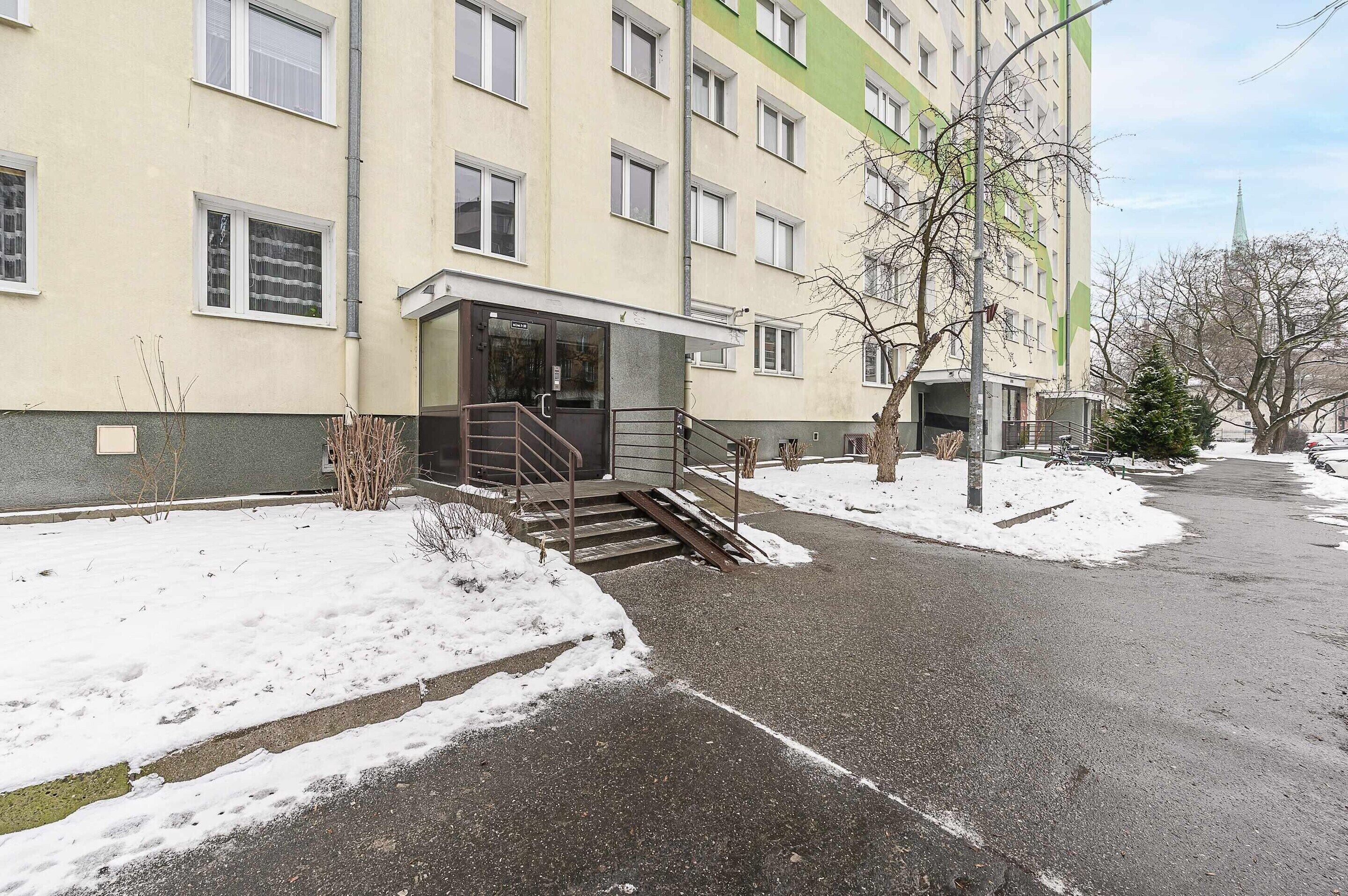 Um edifício de vários andares com fachada plana, um conjunto de degraus que levam à entrada e terreno coberto de neve.