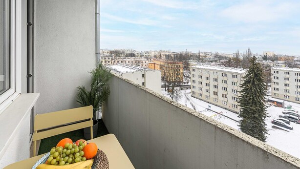 A balcony with a table, a chair, and a fruit basket. - Wola Flat Near City Center (Warsaw)