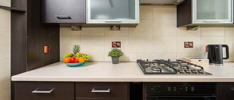Una cocina moderna con armarios oscuros, estufa a gas, horno integrado y encimera con frutero y planta en maceta.
