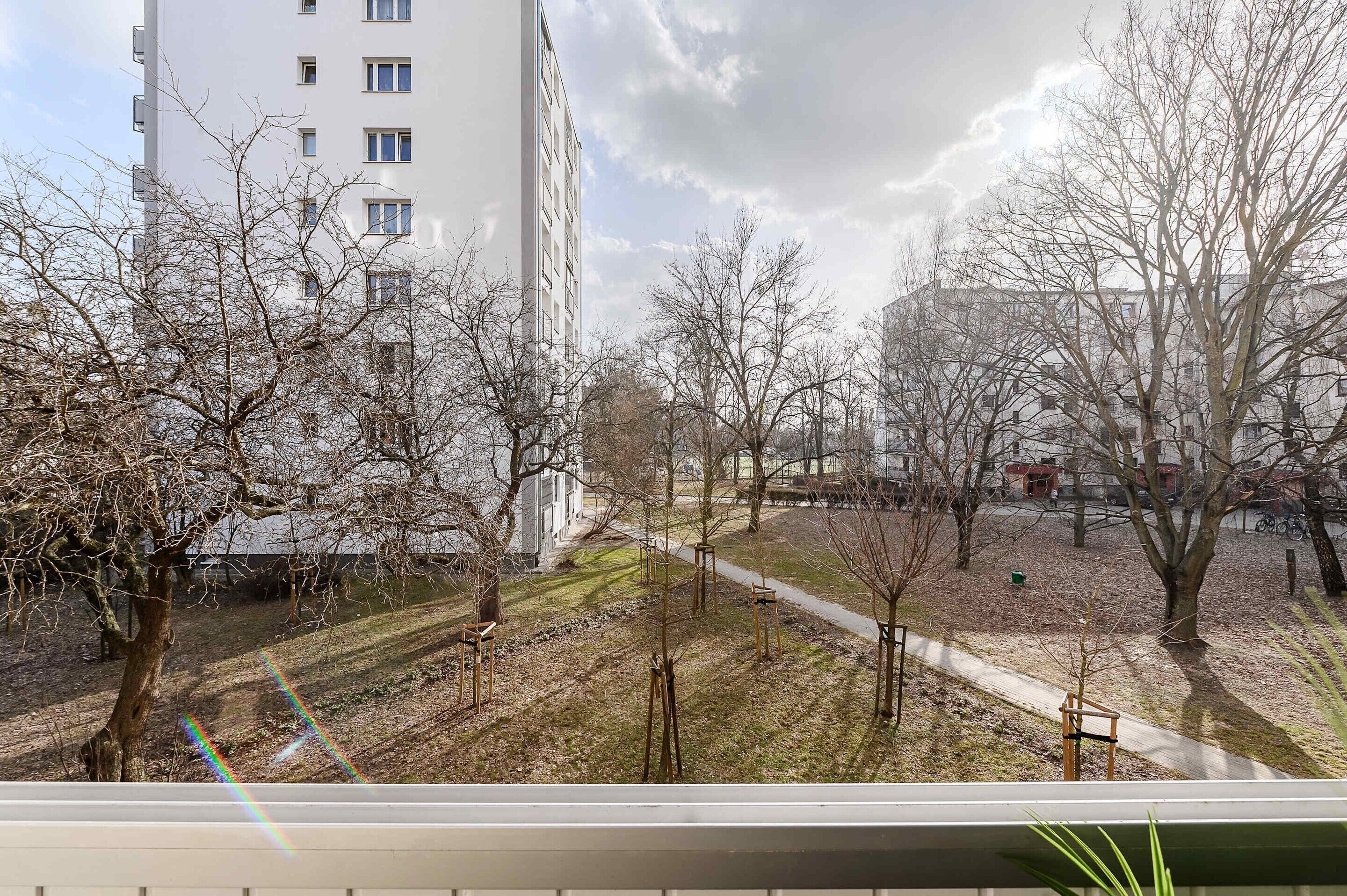 En vy över ett bostadsområde med träd, en gångstig och en hög byggnad i bakgrunden.