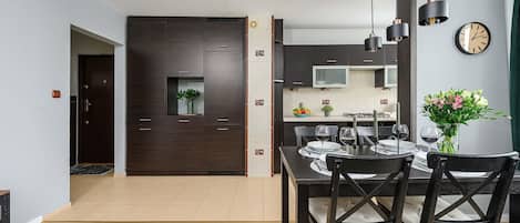 A modern kitchen with dark cabinetry, a dining table set for four, and a clock on the wall.