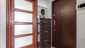 A wooden door with a frosted glass panel, a dark wooden cabinet with drawers, and a small mirror on the wall. - Wola Flat Near City Center (Warsaw)
