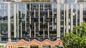 A modern building with a glass facade, multiple floors, and a brick base with signage. - Quiet Flat With Garage (Warsaw)