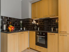 Une cuisine moderne avec des meubles en bois, un crédence en carreaux noirs et un four en acier inoxydable.