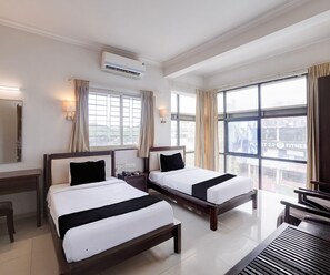 A hotel room with two beds, a desk, a chair, and large windows.