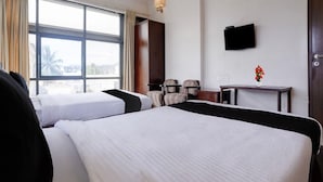 Une chambre d’hôtel avec deux lits, un téléviseur fixé au mur et une fenêtre avec des rideaux.