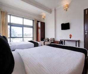 A hotel room with two beds, a TV mounted on the wall, and a window with curtains. - Deluxe Mega Inn (Hospet)