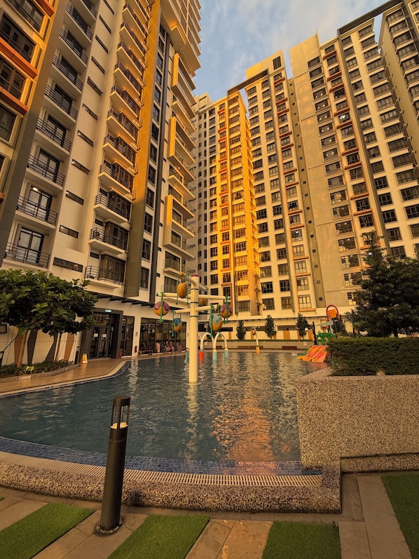 A residential building with a swimming pool, surrounded by greenery and a playground.