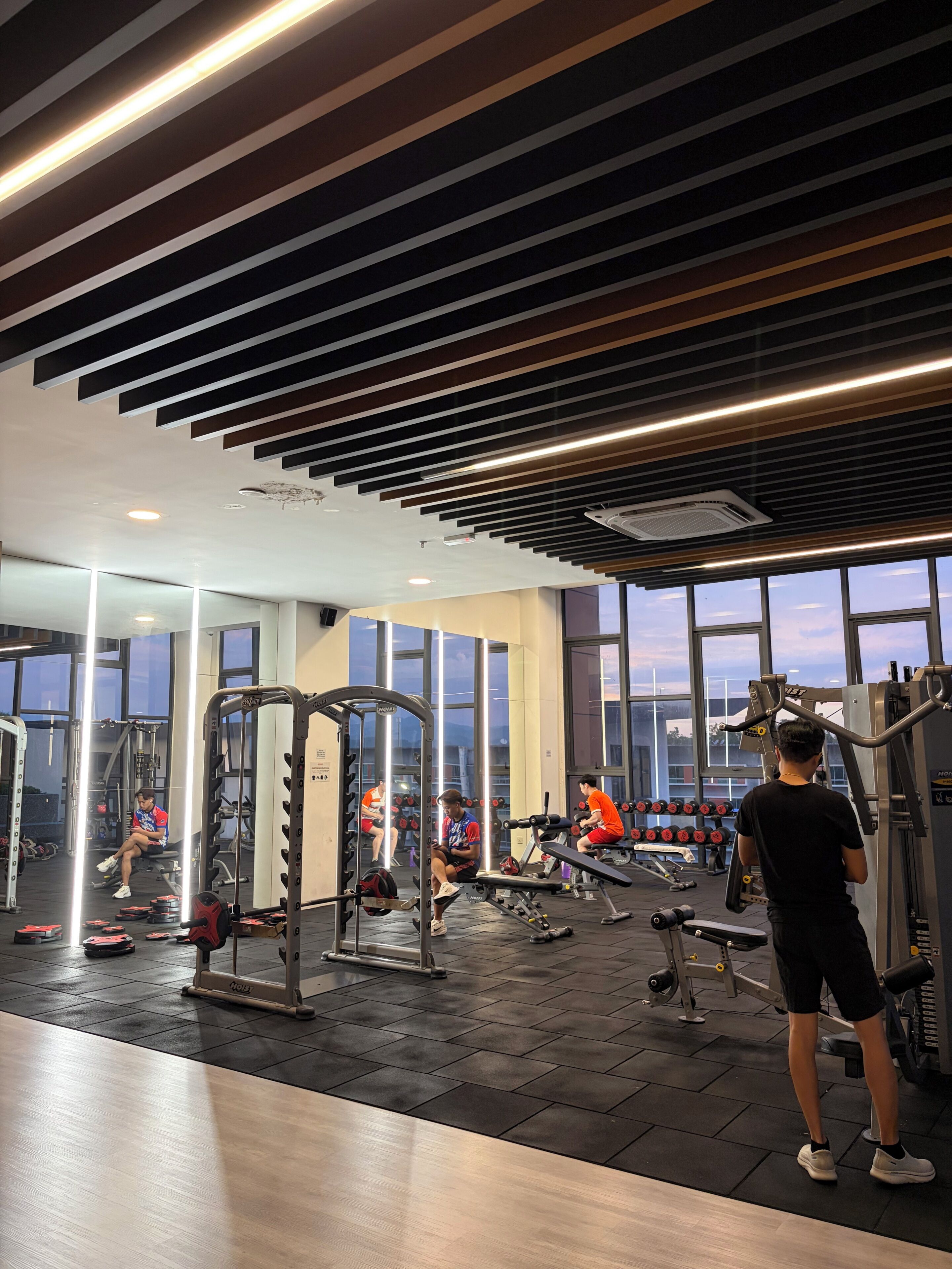 Un gimnasio con diversos equipos de ejercicio, amplias ventanas y un diseño moderno en el techo.
