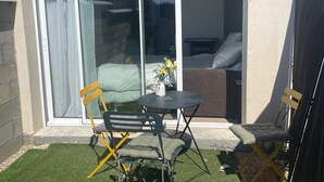A patio area with a sliding glass door leading to a bedroom, two foldable chairs, a small round table, and a vase with flowers.