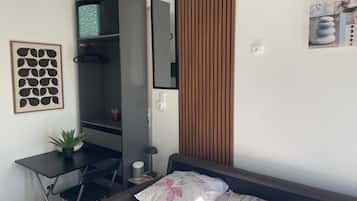 A bedroom with a bed, a desk, a wardrobe, and a potted plant.