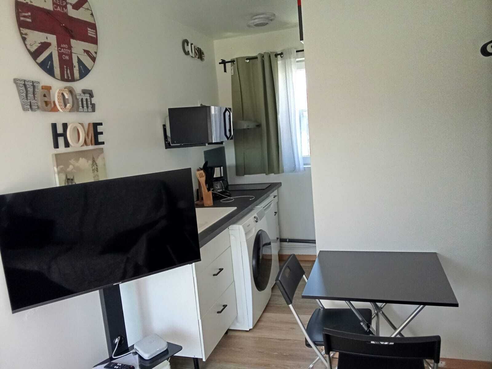 Uma cozinha compacta com máquina de lavar, micro-ondas e televisão de tela plana.