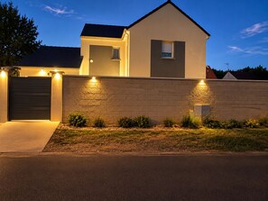 Una casa moderna de dos pisos con garaje, un muro de ladrillo y una entrada bien iluminada.