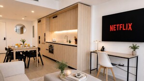 A modern living room with a dining area, kitchenette, and a TV mounted on the wall displaying 'NETFLIX'. - Modern 1BR Stay Near Brickell & Downtown Miami (Miami)